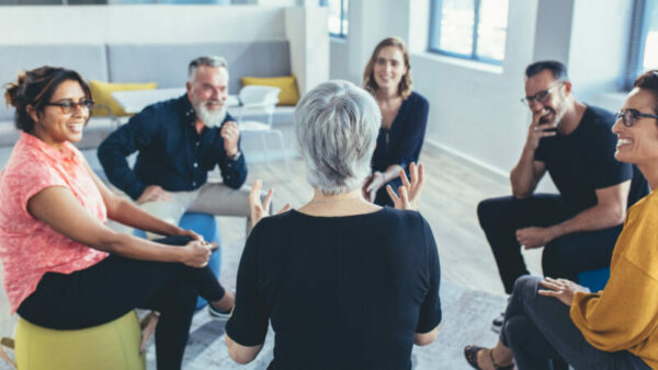 Groep zakenmensen die in een cirkel zitten en discussiëren in het kantoor. Volwassen vrouw die een management training geeft.